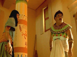Scène du film Astérix et Obélix : Mission Cléopâtre montrant Numérobis dans une maison égyptienne avec une porte située en hauteur sur un mur.